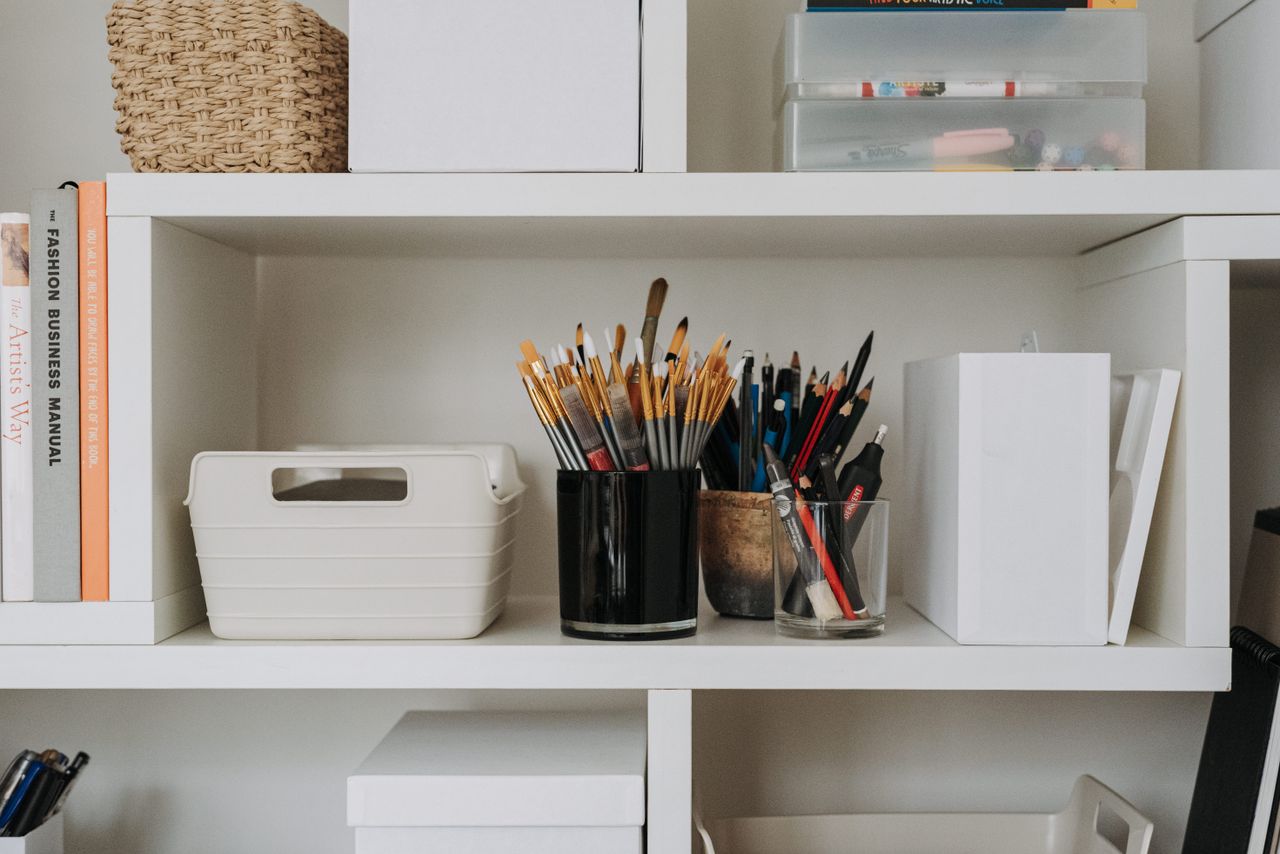 Collection of paintbrushes and pencils placed on white shelf with containers and equipment for painting in modern light art studio